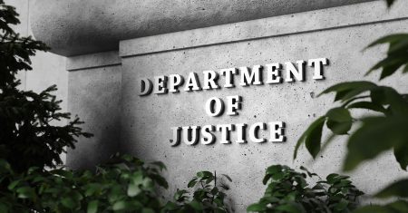 Silver sign of Department of Justice on a classical concrete wall with plants as foreground. Illustration of the concept of enforcement of federal laws