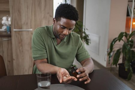 Young black man at home taking his daily medicine with a glass of water